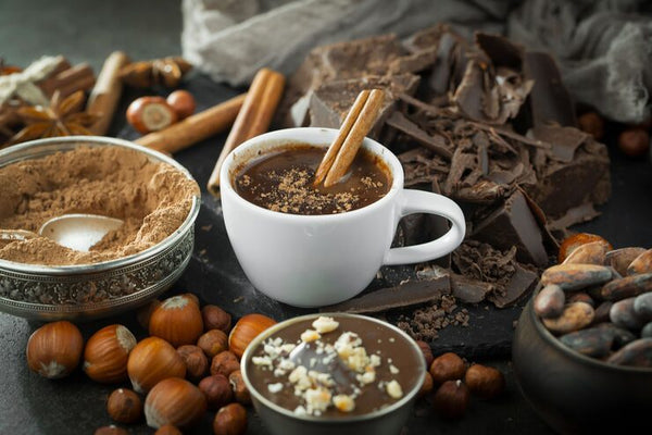 Hot cacao drink with cinnamon sticks, cacao powder, chocolate pieces, and cacao beans, representing premium cacao products and applications