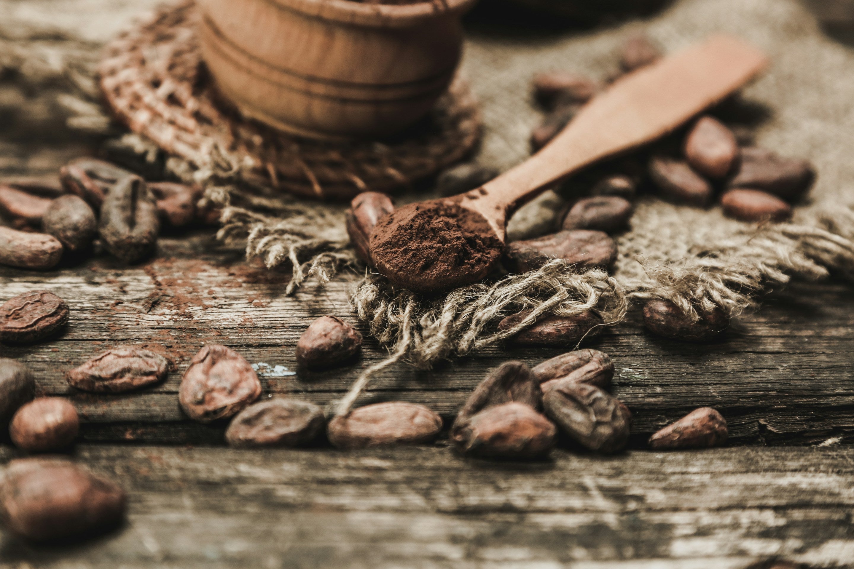 Wooden spoon with cocoa powder surrounded by coffee beans on a rustic wooden surface