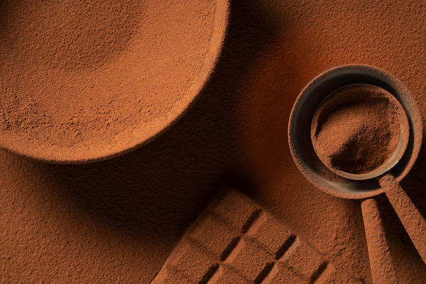 Cocoa powder in a measuring spoon and bowl on a brown textured surface