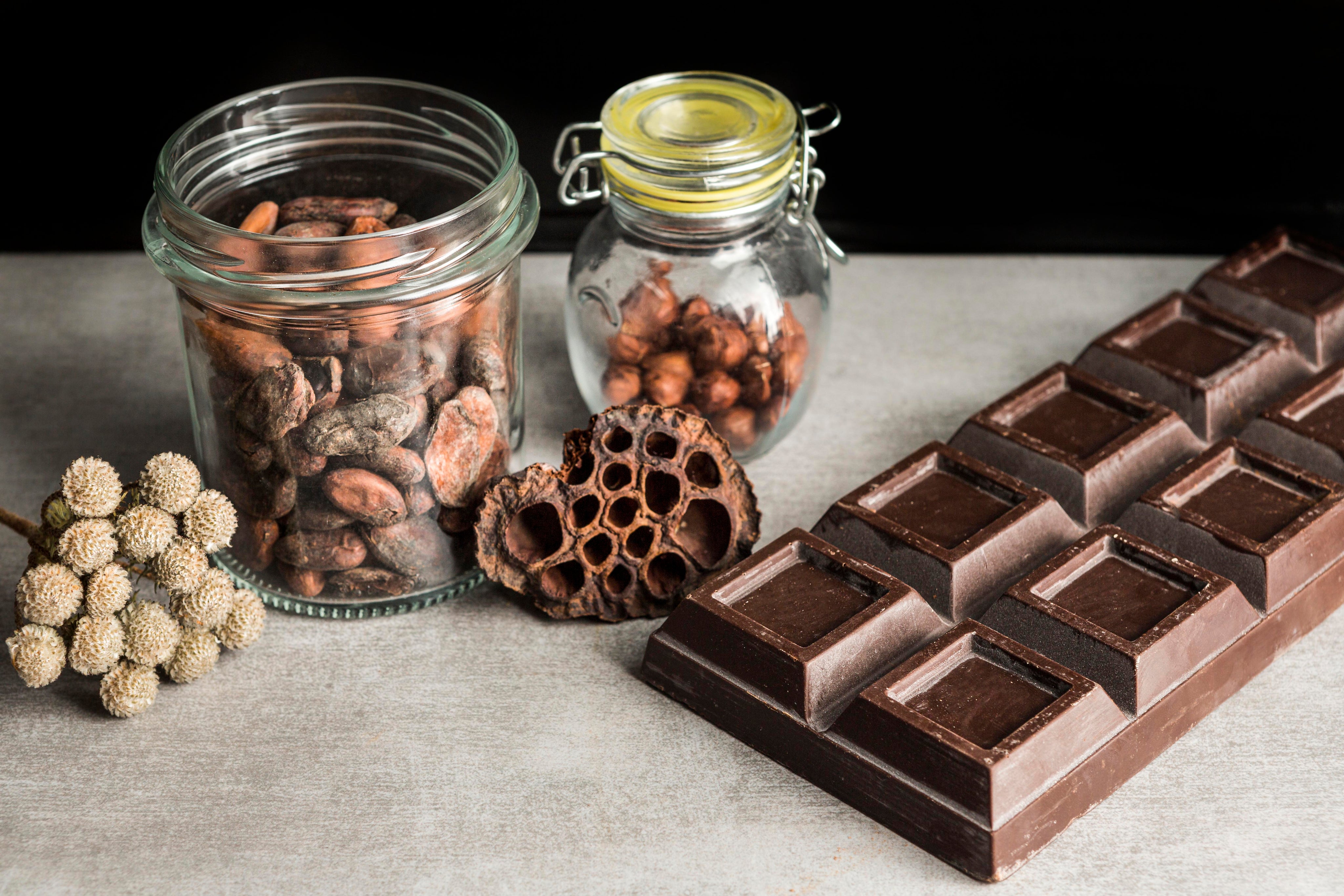 Chocolate bars with jars of nuts and a dried flower on a textured surface